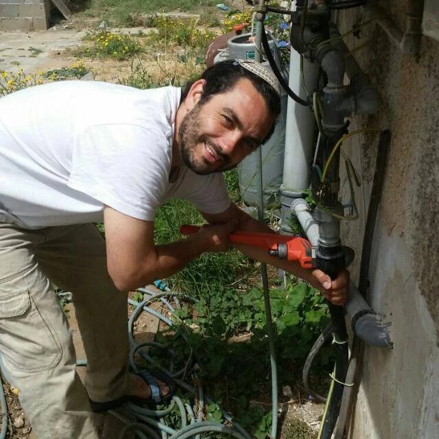 רונן מחייך ומתקן צנרת מים עם מפתח צינורות